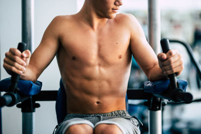 Midsection of shirtless teenage boy exercising at gym