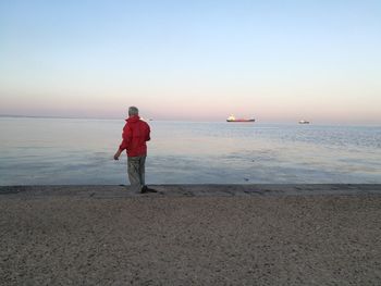 Rear view of man standing on beach against clear sky