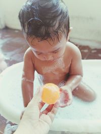 Cropped hand giving ball to shirtless baby boy while having bath