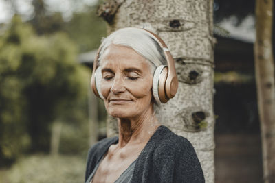 Senior woman relaxing in nature, listening music with headphones