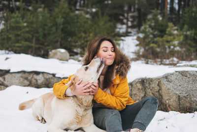 Young smiling woman in yellow jacket with big kind white dog labrador walking in winter forest
