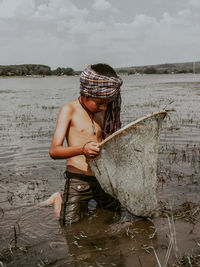 Man holding fishing net by sea against sky