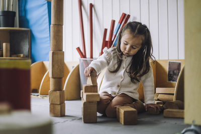 Girl stacking toy blocks while sitting in kindergarten