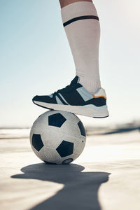 Low section of man holding soccer ball at beach