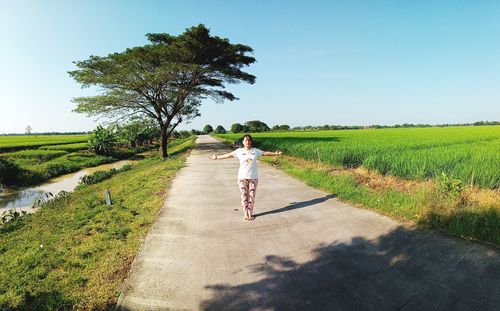 Full length of woman with arms outstretched standing on road against sky