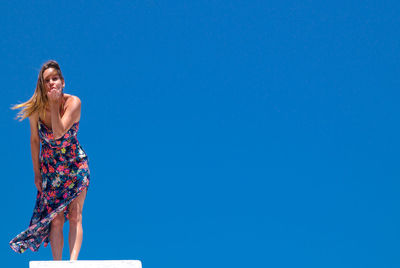 Low angle view of woman blowing kiss while standing against clear blue sky