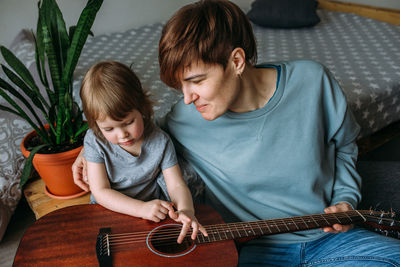 Little girl plays the guitar with her mother on the floor at home