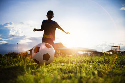 Man playing soccer ball on field against sky during sunset