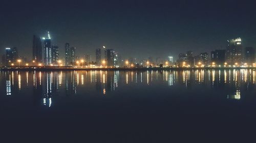 Illuminated buildings by river against sky at night
