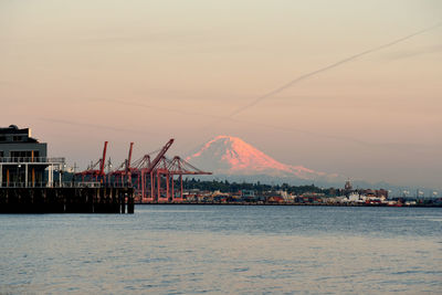 Mount rainier viewed from downtown seattle waterfront with port shipping cranes at dusk.