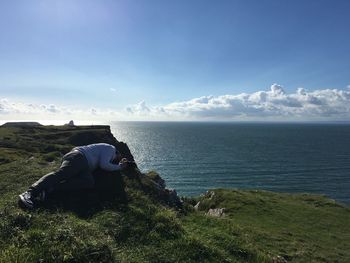 Man relaxing on field by sea against sky