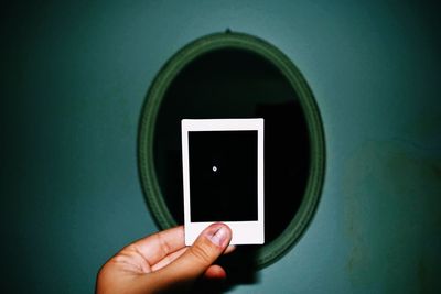 Cropped hand of person holding paper against mirror on wall