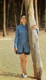 Portrait of young woman standing by tree trunk