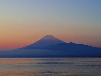 Scenic view of sea by silhouette mountains against sky during sunset
