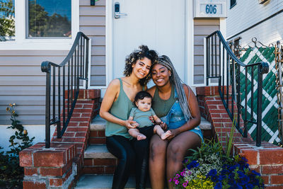 Portrait of smiling lesbians with cute baby boy sitting outside house