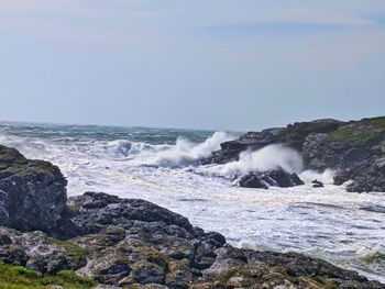 Waves splashing on rocks at shore against sky