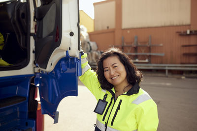 Portrait of smiling female worker opening door of truck outside industry