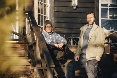 Portrait of mature man in warm clothing sitting by friend on steps