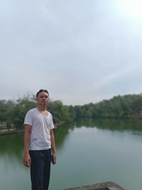 Portrait of young man standing by lake against sky