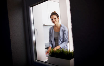 Portrait of smiling young woman at home seen through window