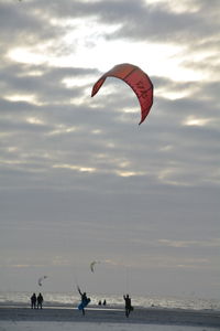 People flying kites at beach against cloudy sky