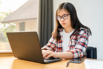 Young woman using mobile phone while sitting on table