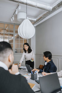 Female entrepreneur distributing adhesive notes to colleagues sitting in meeting room at office