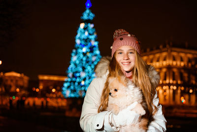 Cute girl holds spitz in her arms in evening on street in light of street