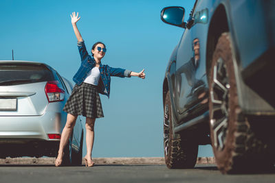 Full length of woman standing by car against sky