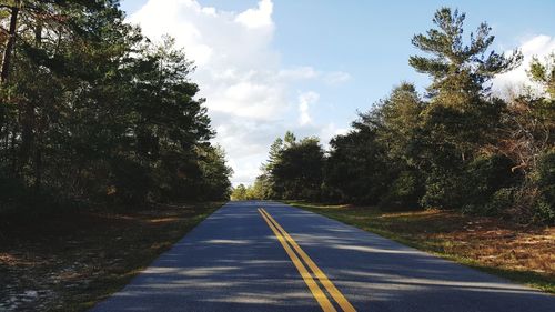 Empty road amidst trees against sky