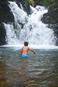 Rear view of shirtless boy splashing water in waterfall