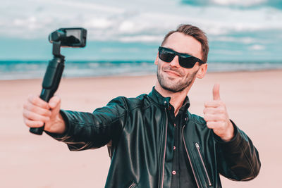 Smiling young man wearing sunglasses filming with video camera at beach