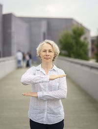 Portrait of woman gesturing while standing on footpath against buildings