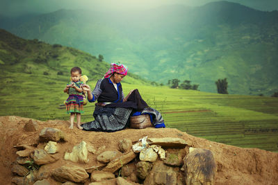 Woman with daughter sewing fabric on rock