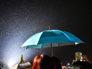 Rear view of people on wet umbrella at night