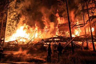 Rear view of firefighters standing by burning house at night