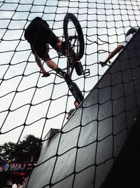 Low angle view of man performing stunt with bicycle seen through fence
