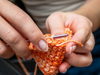 Hands holding a crochet hook working on a pumpkin orange colored piece of arts.