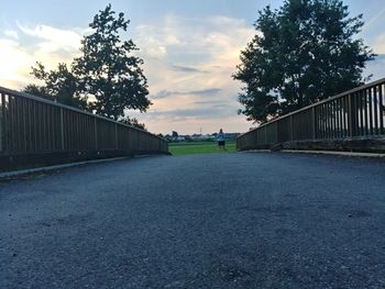Road by trees against sky during sunset