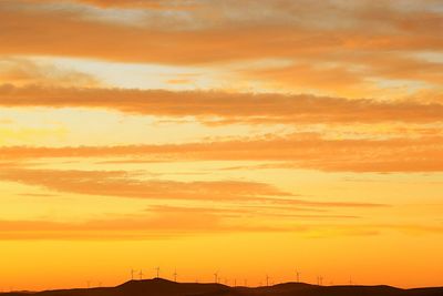 Silhouette windmills on mountains against orange sky