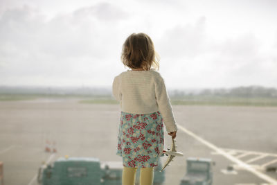 Rear view of child looking at airport runway against sky