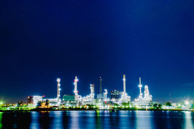 Illuminated factory against blue sky at night