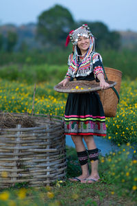 Smiling woman in traditional clothing holding straw basket standing at farm