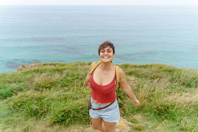 Rear view of woman standing on grassy field against sea