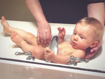 Midsection of mother giving bath to baby boy in sink