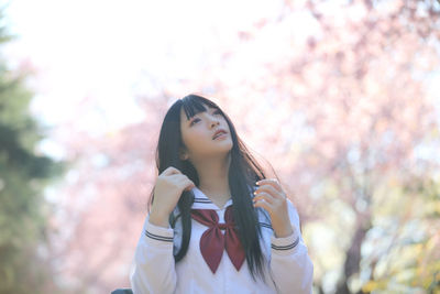 Portrait of beautiful young woman standing against trees