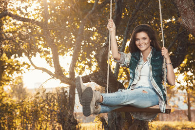 Smiling woman sitting on swing in park