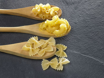 Various pasta in wooden spoons on slate
