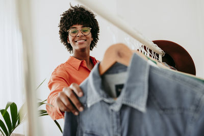 Smiling businesswoman wearing eyeglasses holding clothes at home office