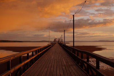 Pier leading to sea against cloudy sky